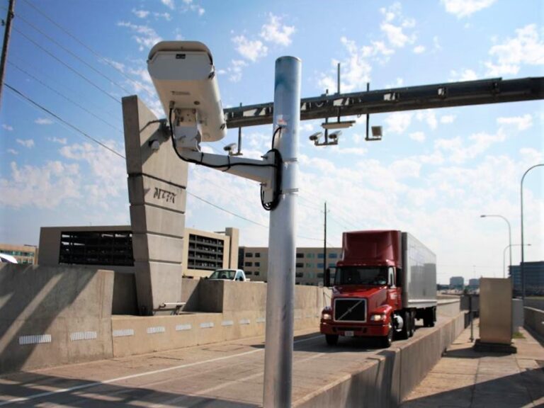 Truck passing an open-road tolling point with ANPR camera pole and overhead ETC gantry