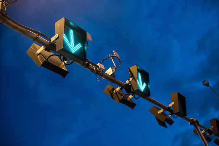 Low-angle view of overhead lane control signals showing green downward arrows on a gantry at dusk