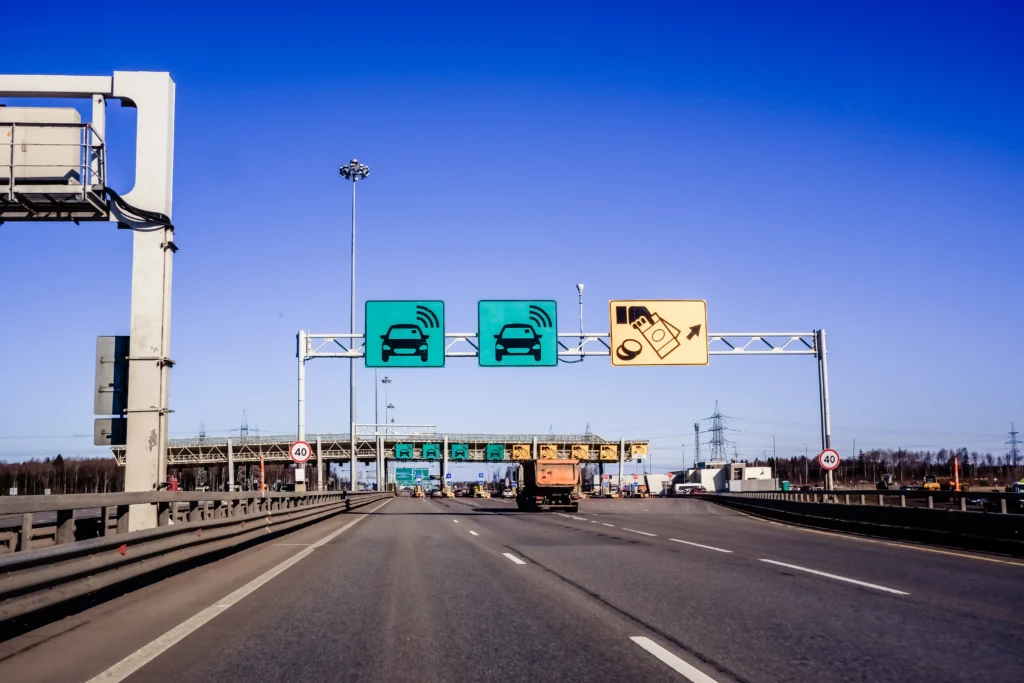 Highway approaching a toll plaza with overhead lane signs for electronic toll collection and payment